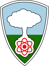 A shield with a white mushroom cloud rising from a red atom against a blue sky