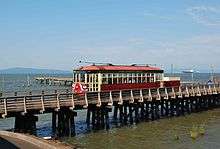 The streetcar passing over a low wooden trestle connected to a dock on the Columbia River