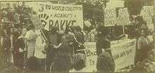 a monochrome photo of a protest rally. Many of the protesters are minorities, and have Afro hairstyles. "WOMEN AGAINST BAKKE" is a typical sign being held.