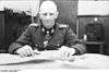 A man stiing at a desk, wearing a military uniform and neck order, in the shape of a cross.