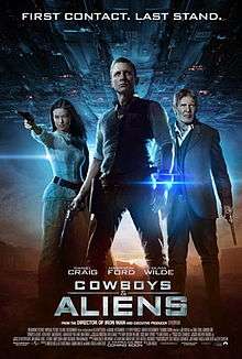 A man wearing a metal bracelet glowing a blue light on his left wrist, with a revolver in his right hand. To the left, a woman aiming a revolver. To the right, an older man wielding a revolver. In the background, a large metal object over a desert landscape. Above is shown "FIRST CONTACT. LAST STAND." Below them are the names of Daniel Craig, Harrison Ford, and Olivia Wilde above the title "COWBOYS & ALIENS", film credits, and theatrical release date.