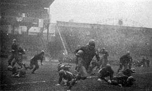 A player with a football runs past others.