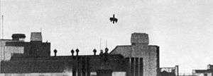 A picture of an aircraft, minus its tailplane and outer wing tips diving onto a rail station