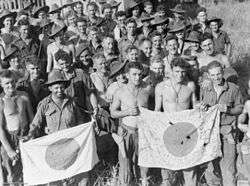 Men wearing military uniforms including jungle greens and slouch hats, display Japanese flags