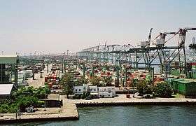 Harbor dock, with many rows of containers, and large cranes for loading on to ships. The cranes are labeled 'Evergreen.'