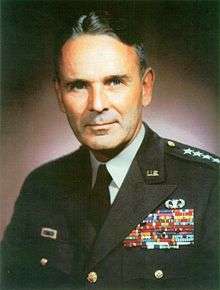Middle-aged man with graying dark hair parted slightly off-center. He wears a green dress uniform, with suit and tie, is clean-shaven, and has four stars on his shoulder to indicate his rank.
