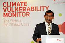 Bespectacled man in a suit speaking at a podium