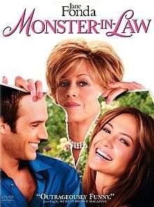 A wedding cake with figurines of the bride and groom. A finger pushes the bride into the cake.