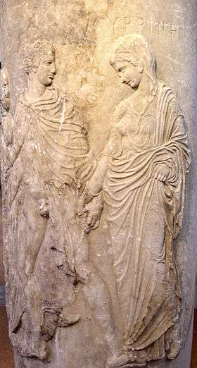 A carving of a noble robed man and woman apparently leading a demure, robed woman. The man's robe is open, exposing his penis. He holds the hand of the woman.