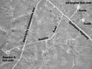Black and white aerial view of several roads through a forest with a few buildings. The image is labeled "Jet engine test cells" in the upper right corner with buildings in two cleared circles at end of small roads labeled "North" and "South". In the lower left corner is a larger building in a cleared area labeled "Reactor & hot cells". The road to this is labeled "Reactor Road" and it leads to the labeled "Quehanna Highway". A clearcut strip is labeled "Electricity transmission line".