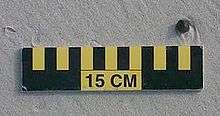 A ball of tar about 1&nbsp;cm (0&nbsp;in) wide on sand above a 15&nbsp;cm (6&nbsp;in) scale
