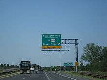 A divided highway curves to the left as the rightmost lane exits underneath an overhead green sign indicating the ramp leads to Worcester Highway and MD&nbsp;589 toward Ocean Pines