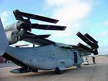 A V-22 with its wing rotated 90 degrees so it runs the length of the fuselage